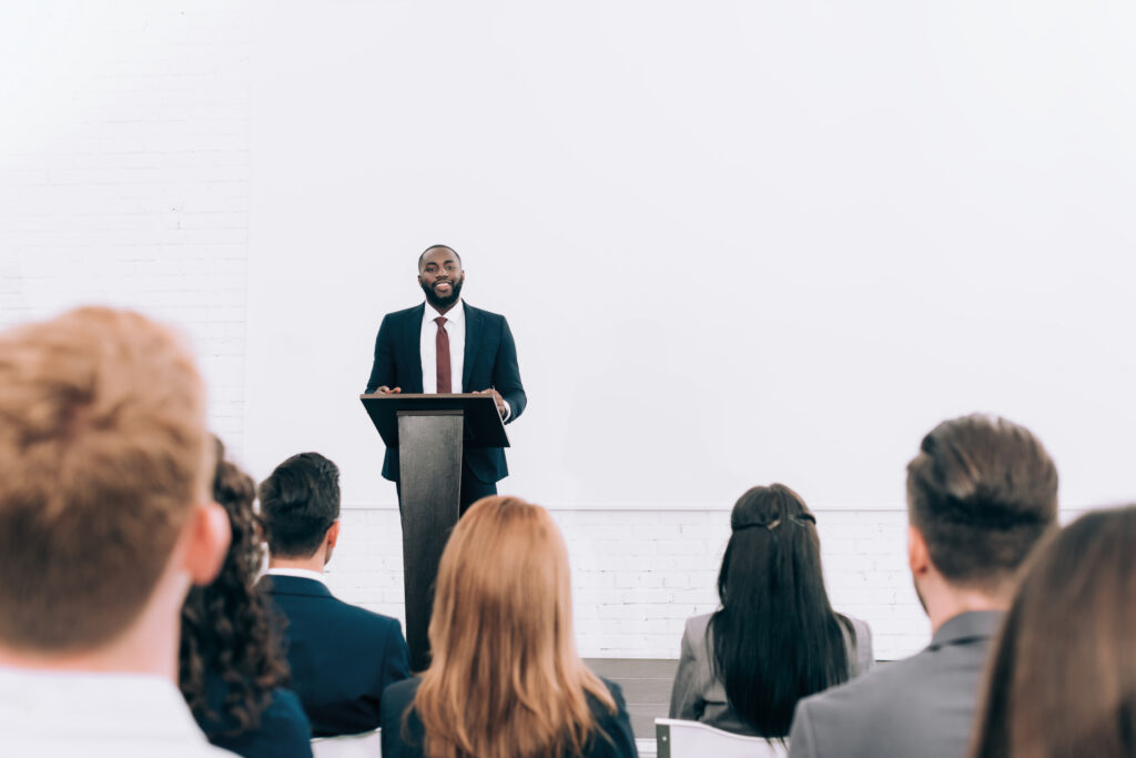 smiling african american lecturer talking to audience during seminar in conference hall